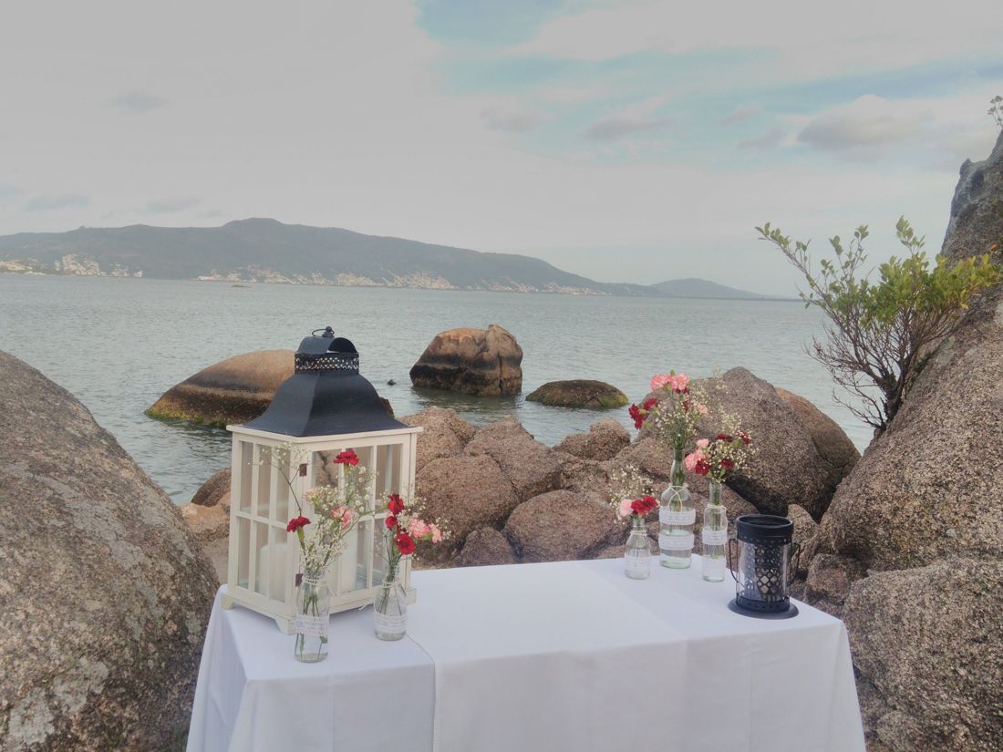 Altar de cerimônia à beira-mar entre as pedras, com lanterna e flores